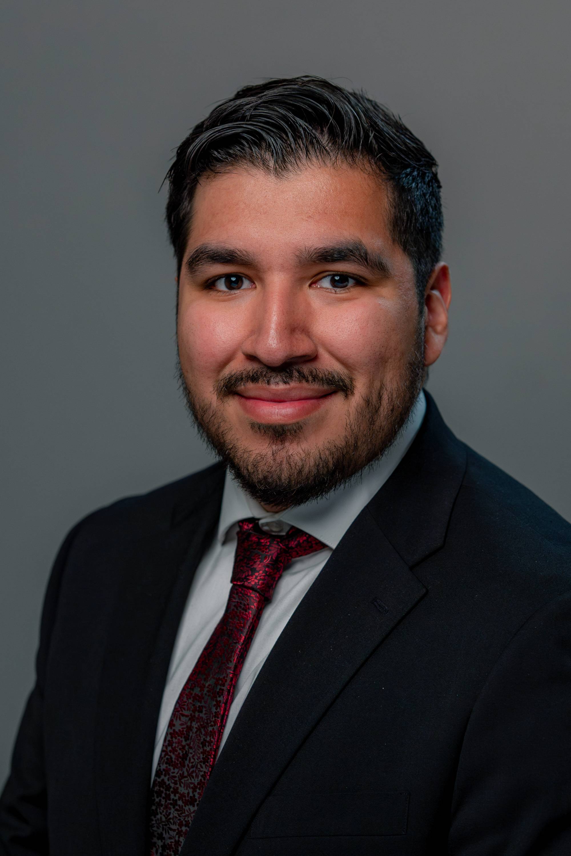 A formal headshot of Diego, wearing a suit with a red tie
